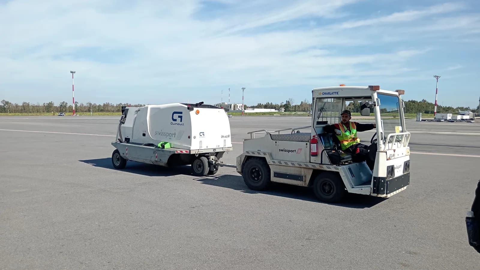 An electric baggage tractor towing carts across an airport apron
