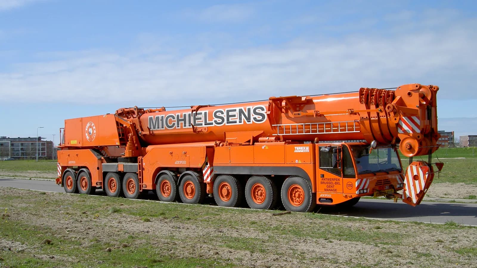 An orange all-terrain mobile crane with its boom lowered, parked on a grass lot