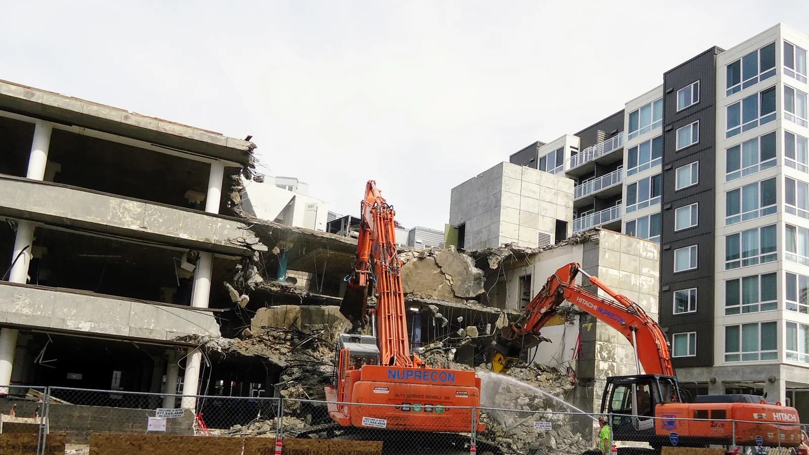Une pelle mécanique orange démolissant un bâtiment de béton à côté d'un immeuble
