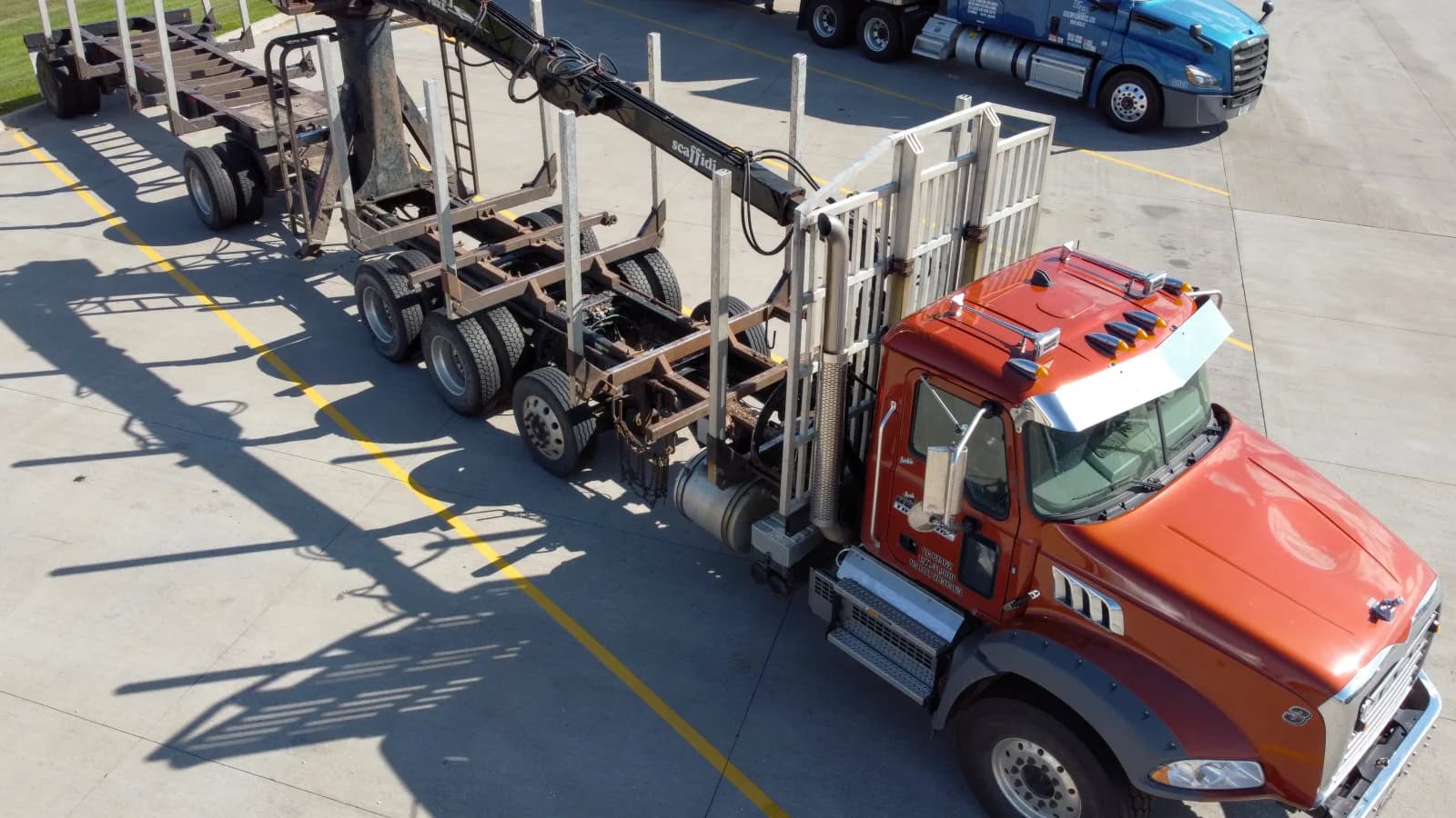 An aerial view of a red log truck with an empty trailer parked in a yard
