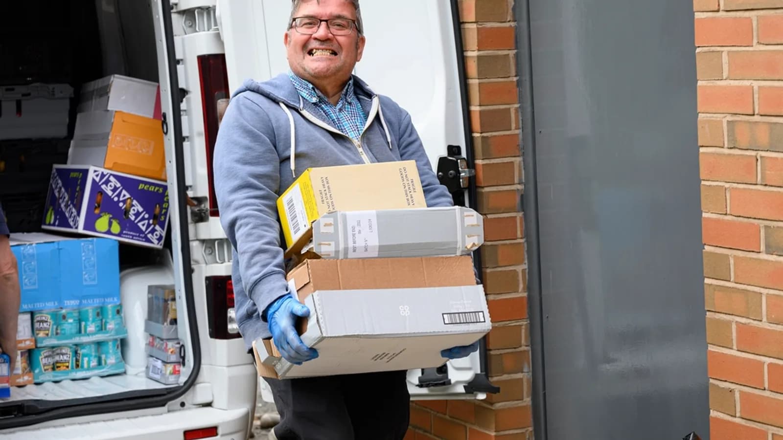 Un livreur transportant des boîtes de la porte latérale d'un fourgon jusqu'à une porte d'entrée