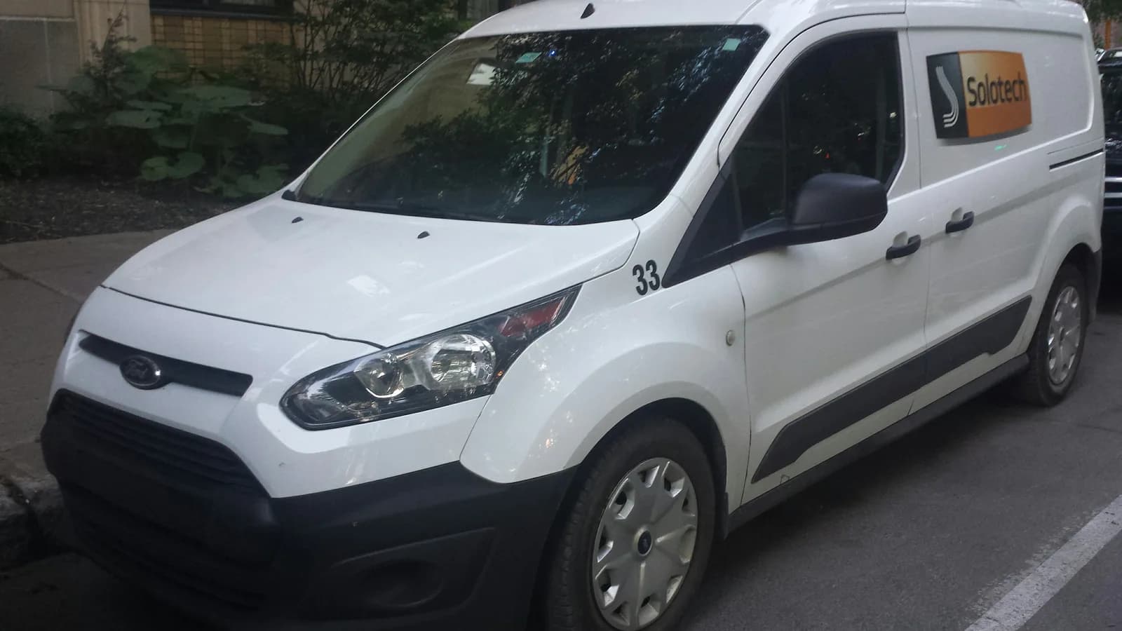 A white compact courier van parked in front of a building