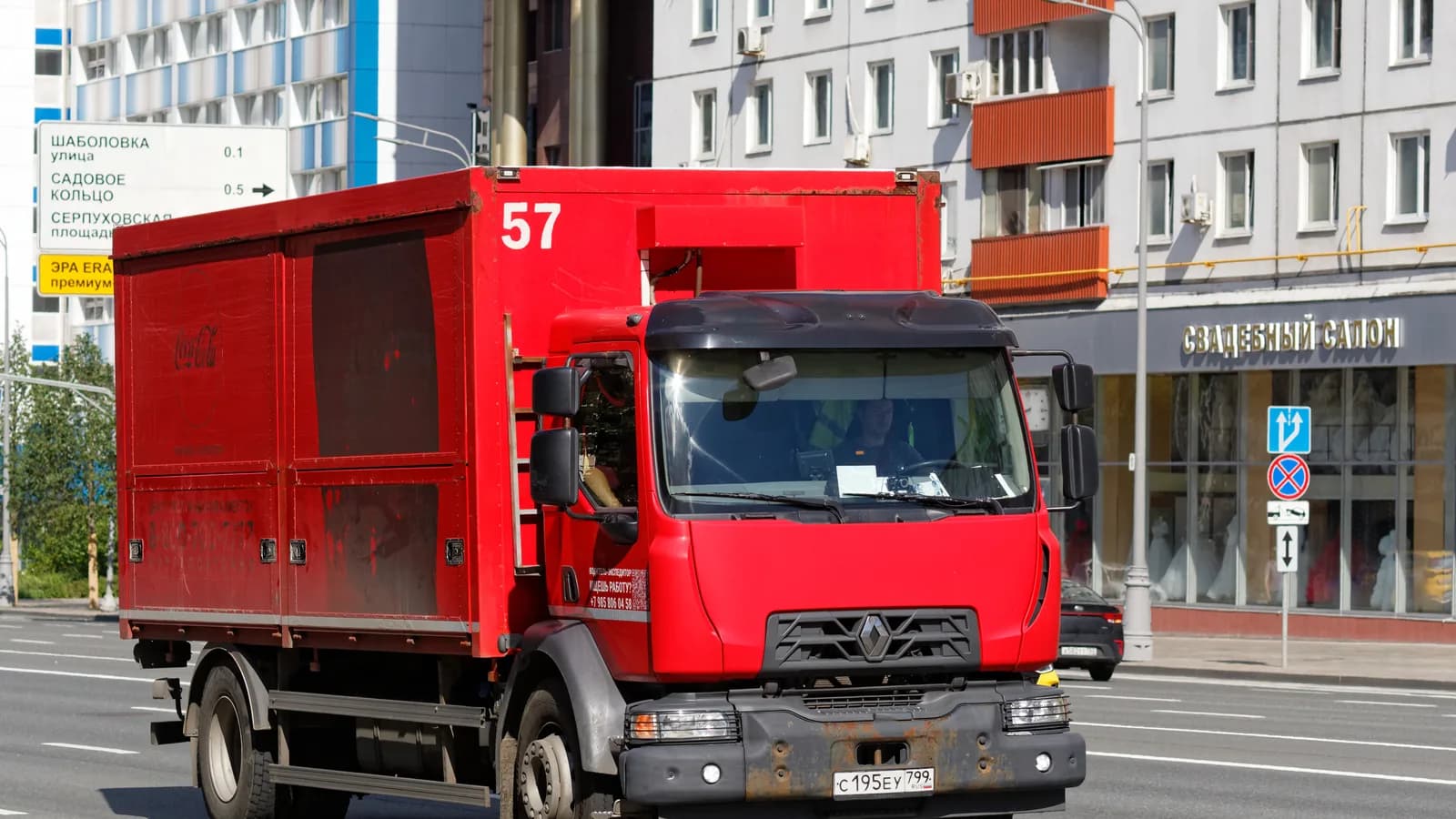 A red box truck driving along a city street past apartment buildings