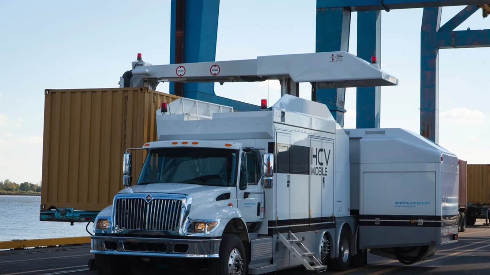 A container truck passing under a gantry crane at a port terminal