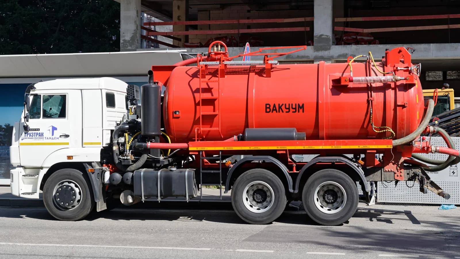 A red vacuum tank truck parked beside a building with its hoses coiled