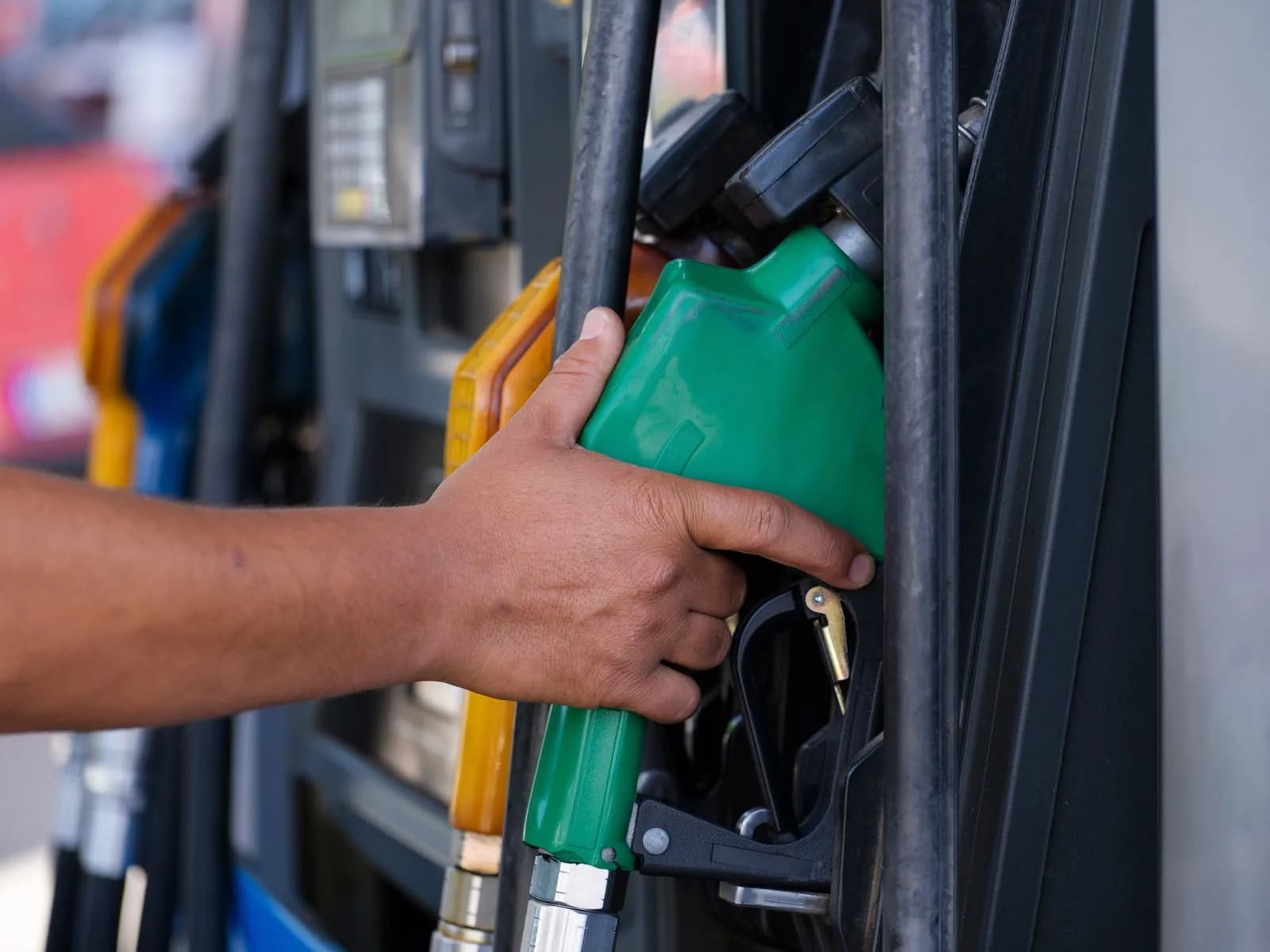 A hand holding a green fuel nozzle at a gas station pump