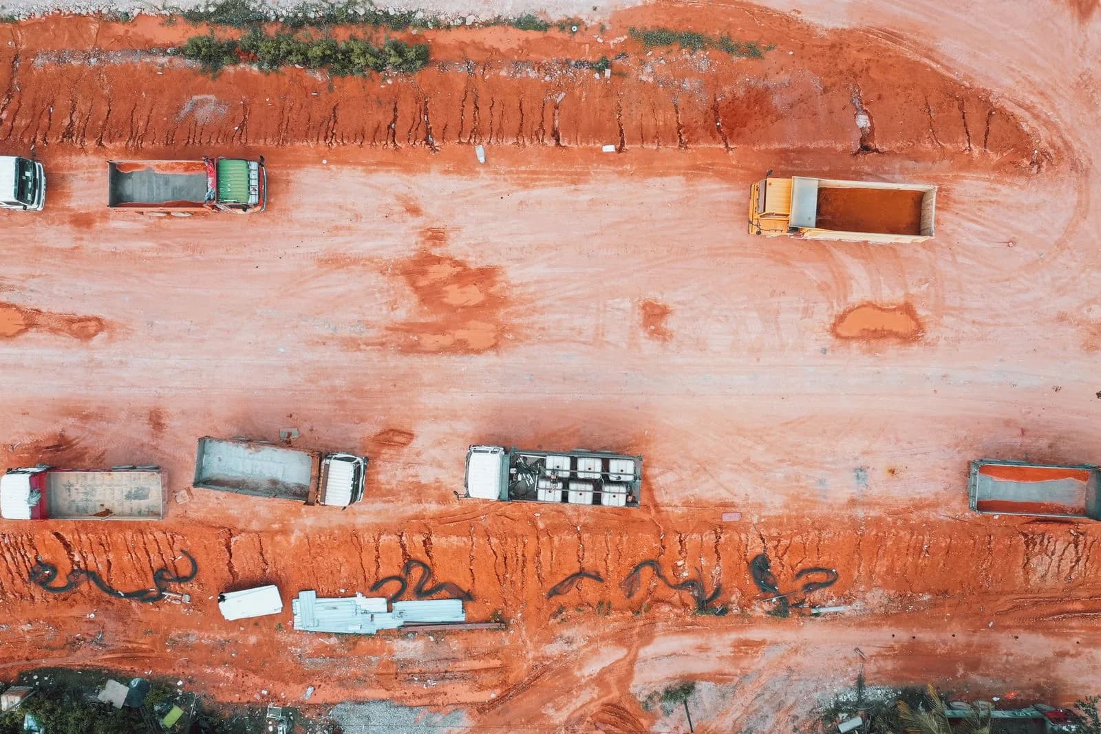 An aerial view of trucks on a construction site with orange soil and earthworks