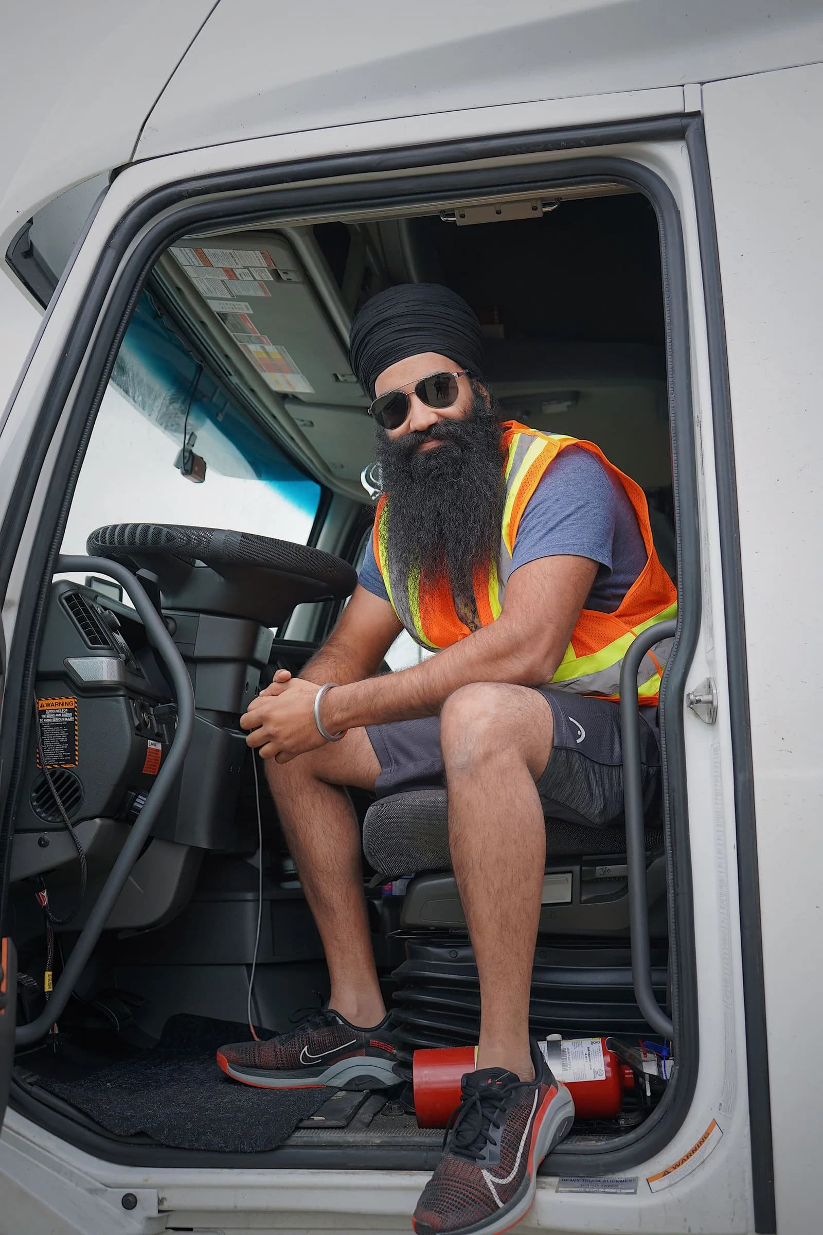 A truck driver in a safety vest sitting in his truck's open cab door