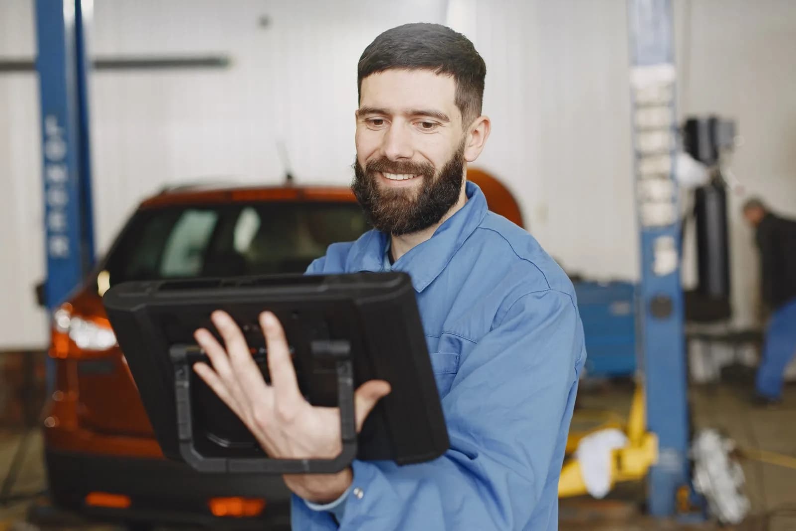 A smiling mechanic using a digital diagnostic tablet in a garage