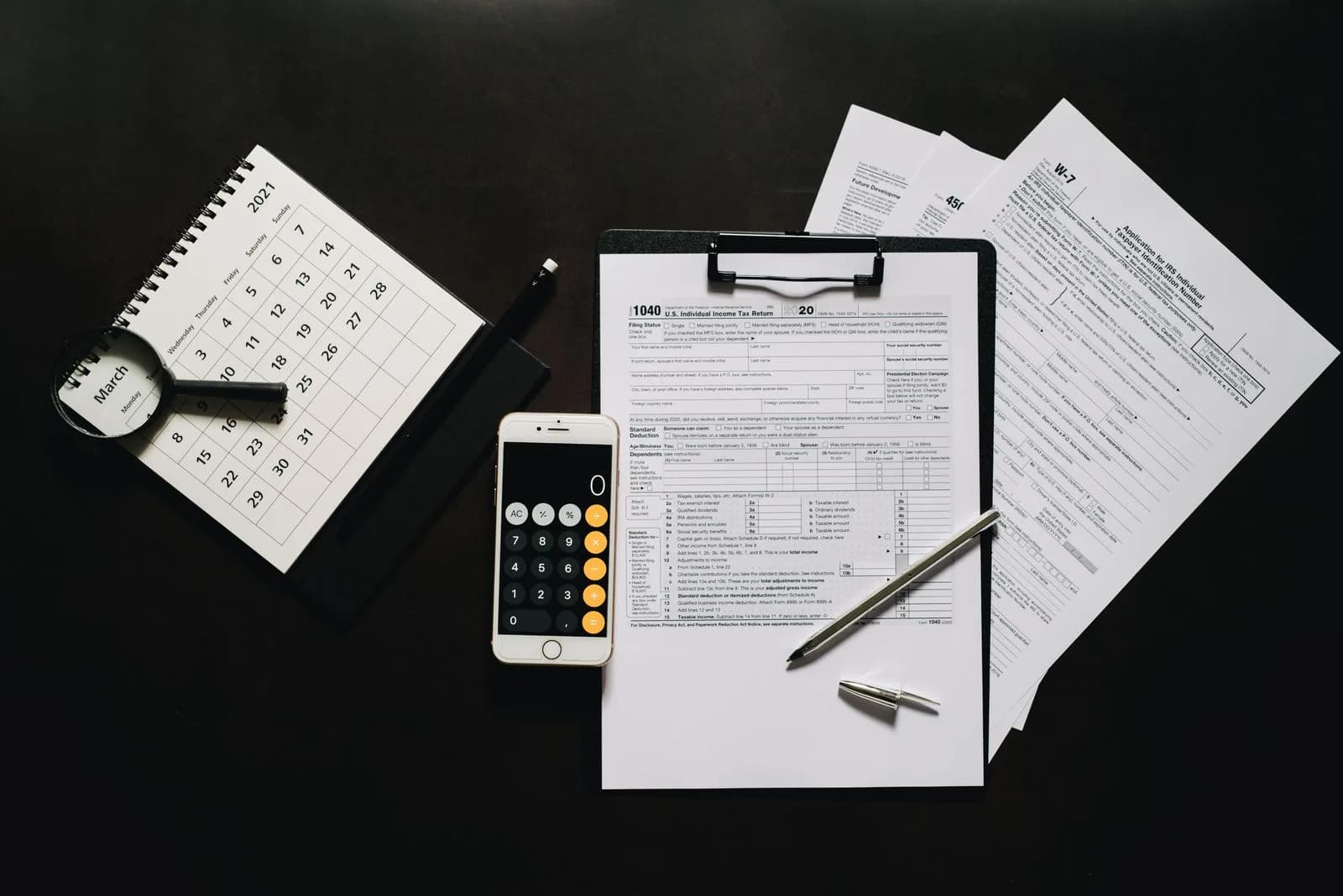 Tax forms, a calculator, and a calendar laid out on a desk
