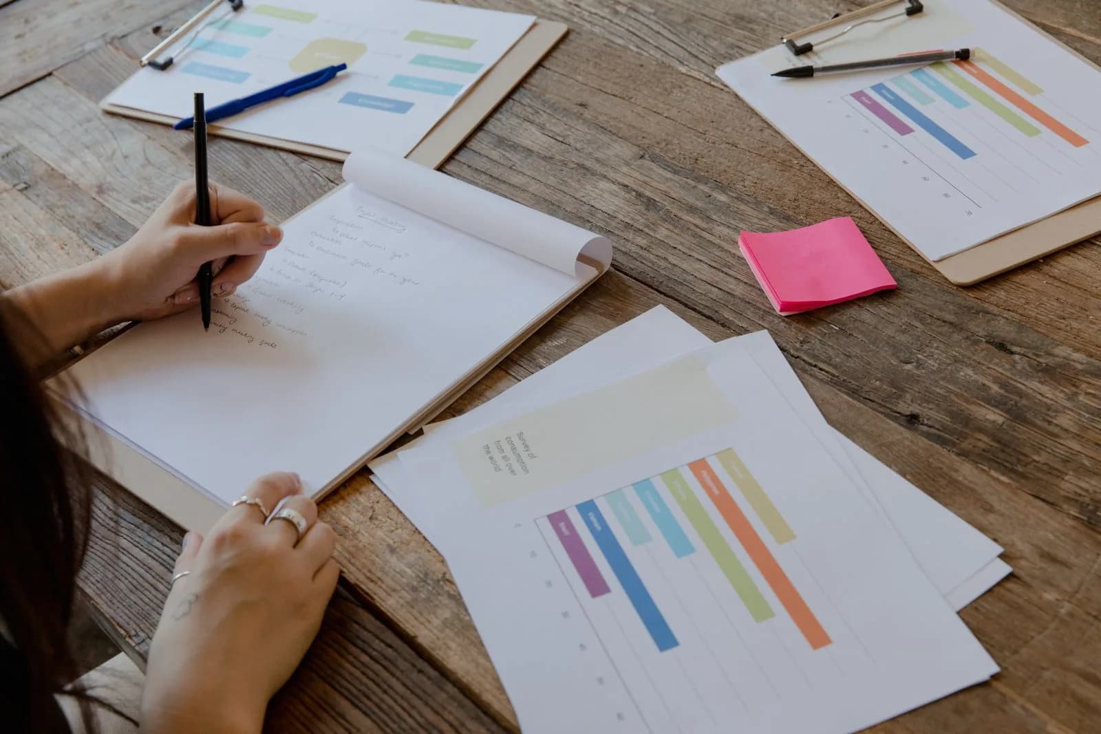 A person reviewing planning documents and charts spread across a wooden desk
