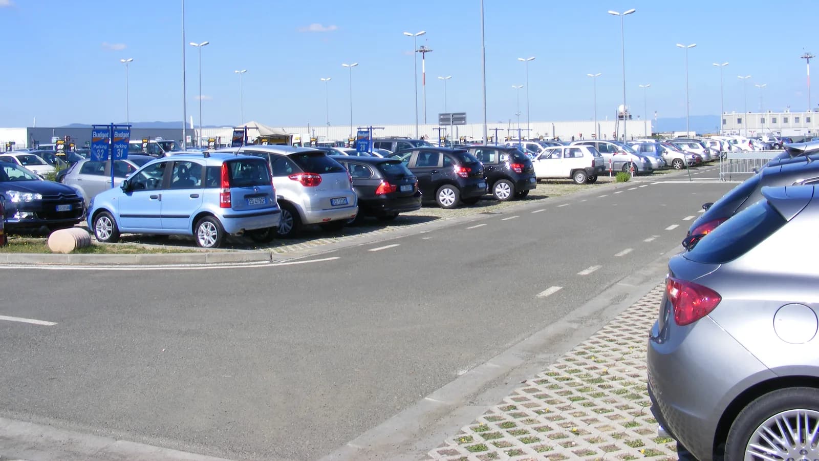 Rows of cars parked in a rental lot beside an airport under a clear sky