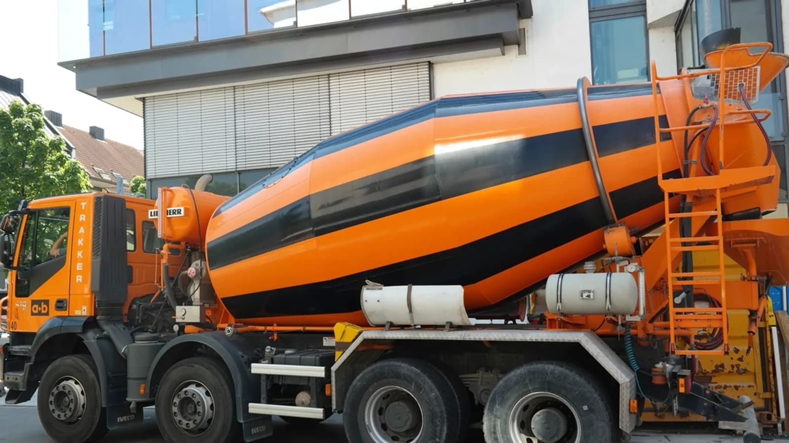 An orange ready-mix concrete truck with a striped drum parked beside a building on a city street