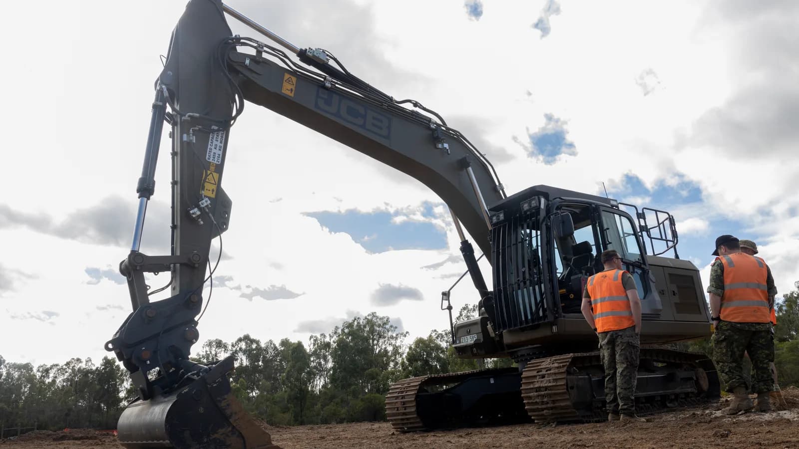 An excavator on a work site with technicians standing beside it