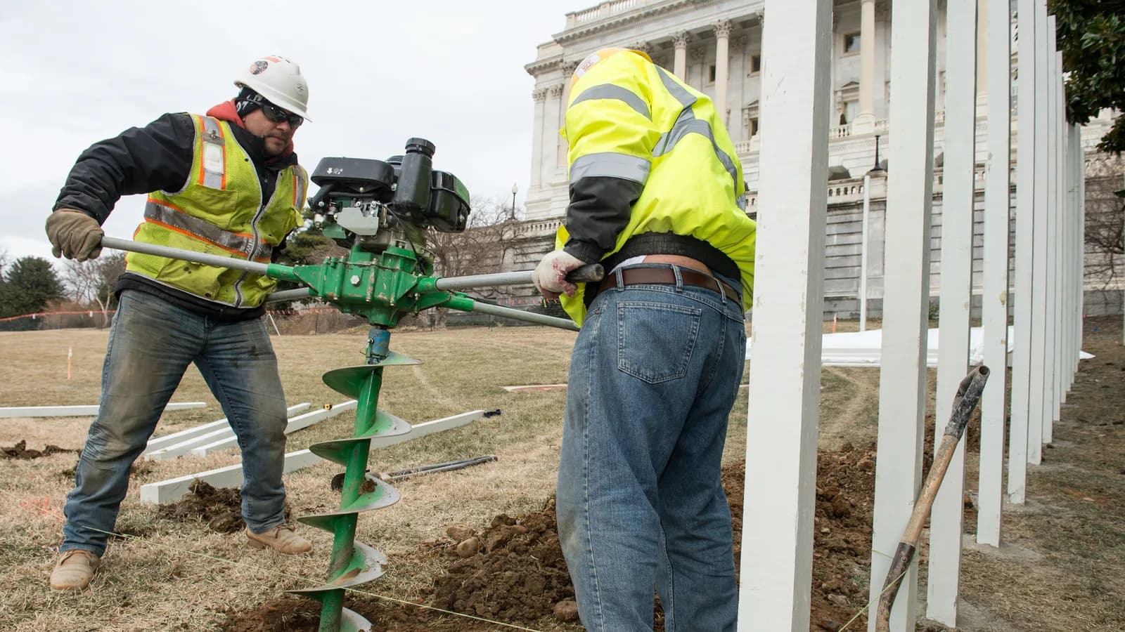 A crew in safety vests setting fence posts with an auger