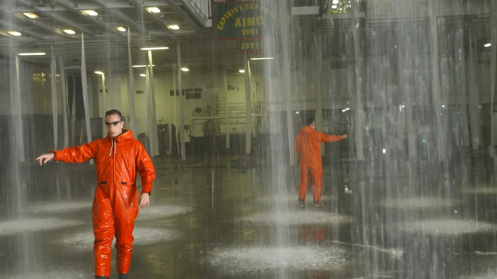 A worker in a red suit standing under a discharging sprinkler system