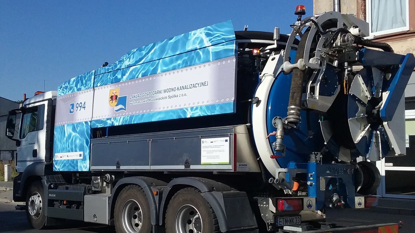 A vacuum excavation truck with its suction boom raised on a city street