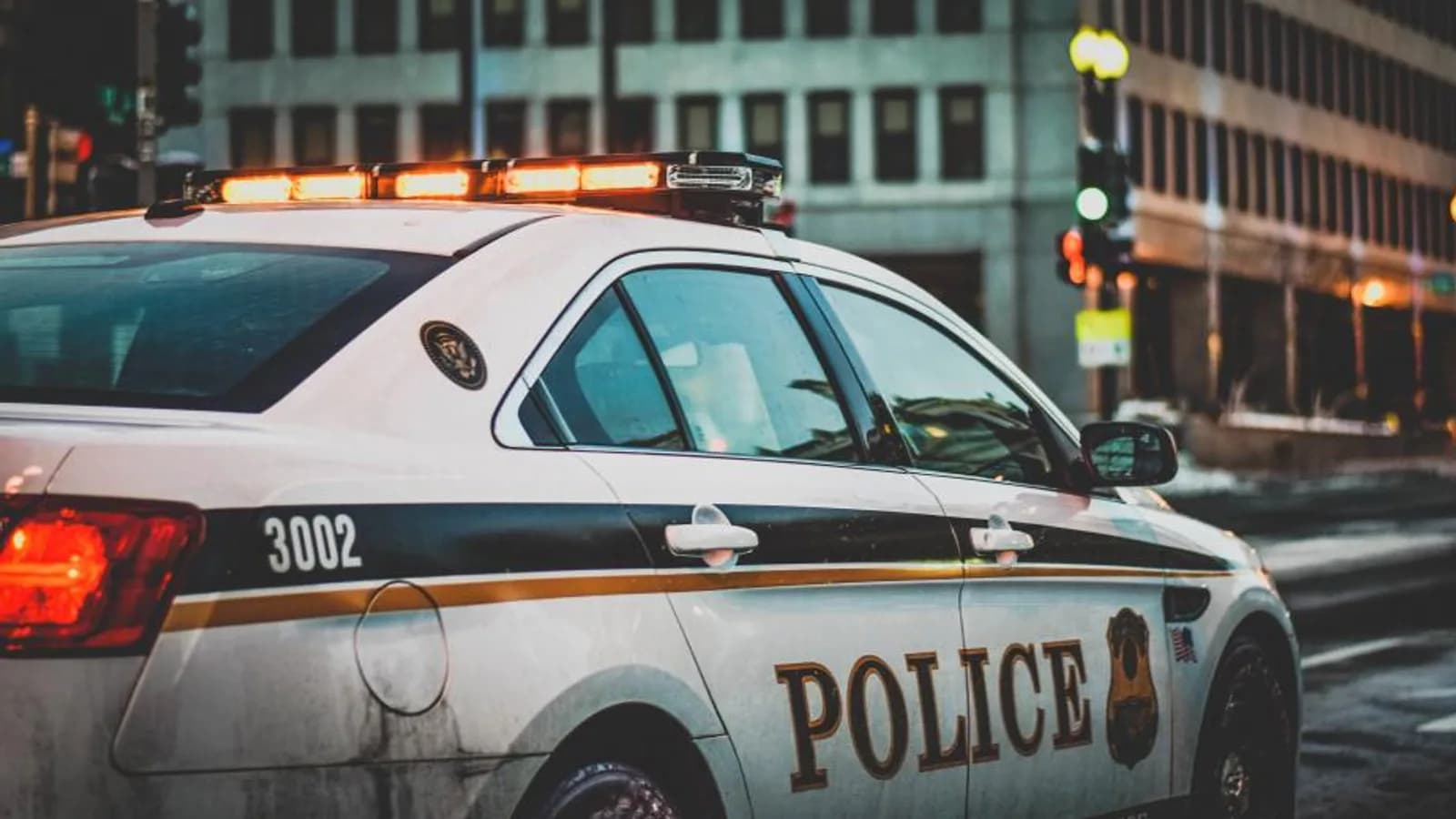 A police patrol car with its light bar on at a city intersection