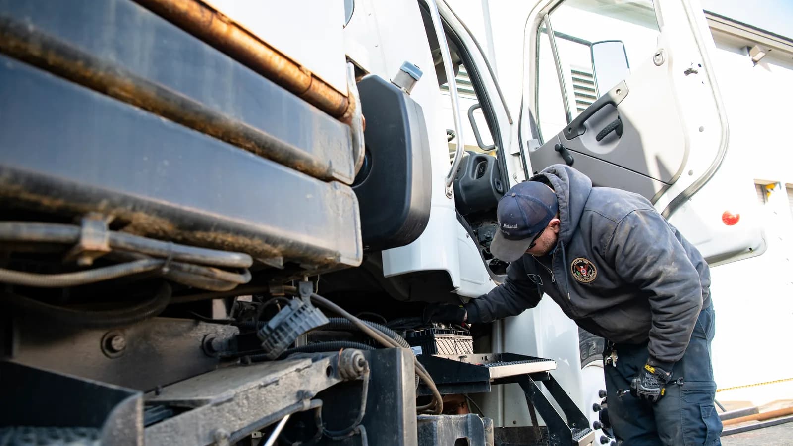 A mechanic working on the engine of a heavy truck from a step