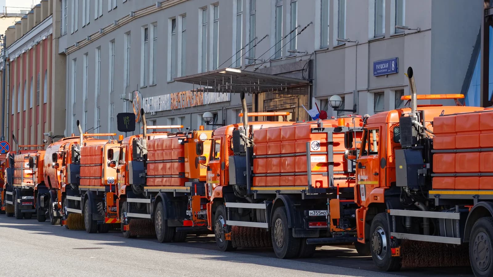 A row of orange municipal dump trucks parked along a city street