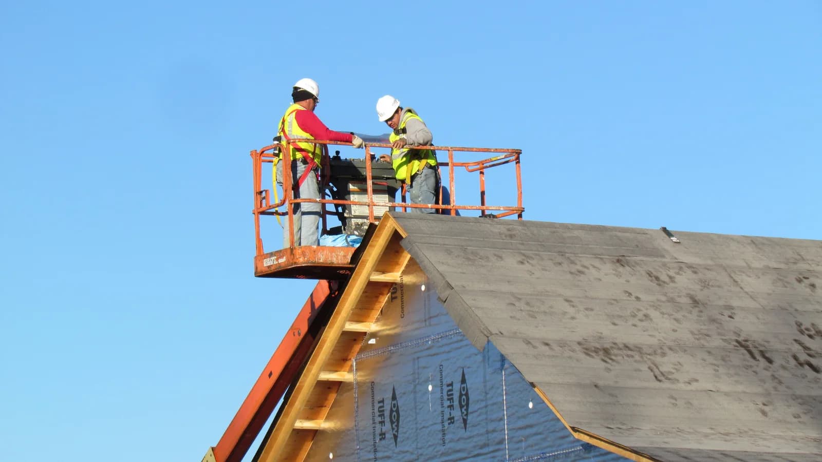 A roofing crew on a lift platform at the edge of a roof under construction