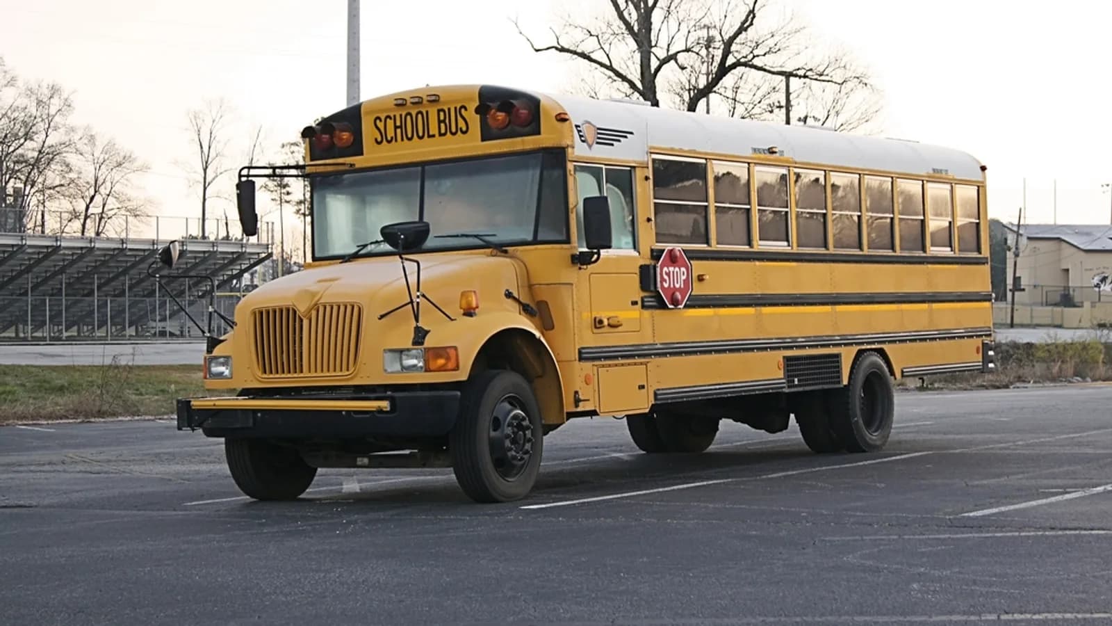 A yellow school bus parked in an empty lot beside a sports field on a clear day