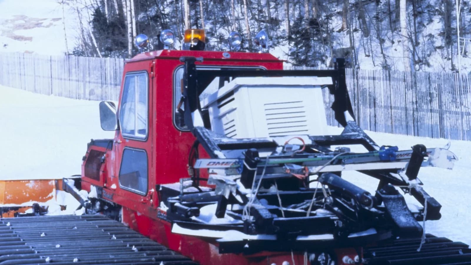 A red snowcat groomer on a ski slope