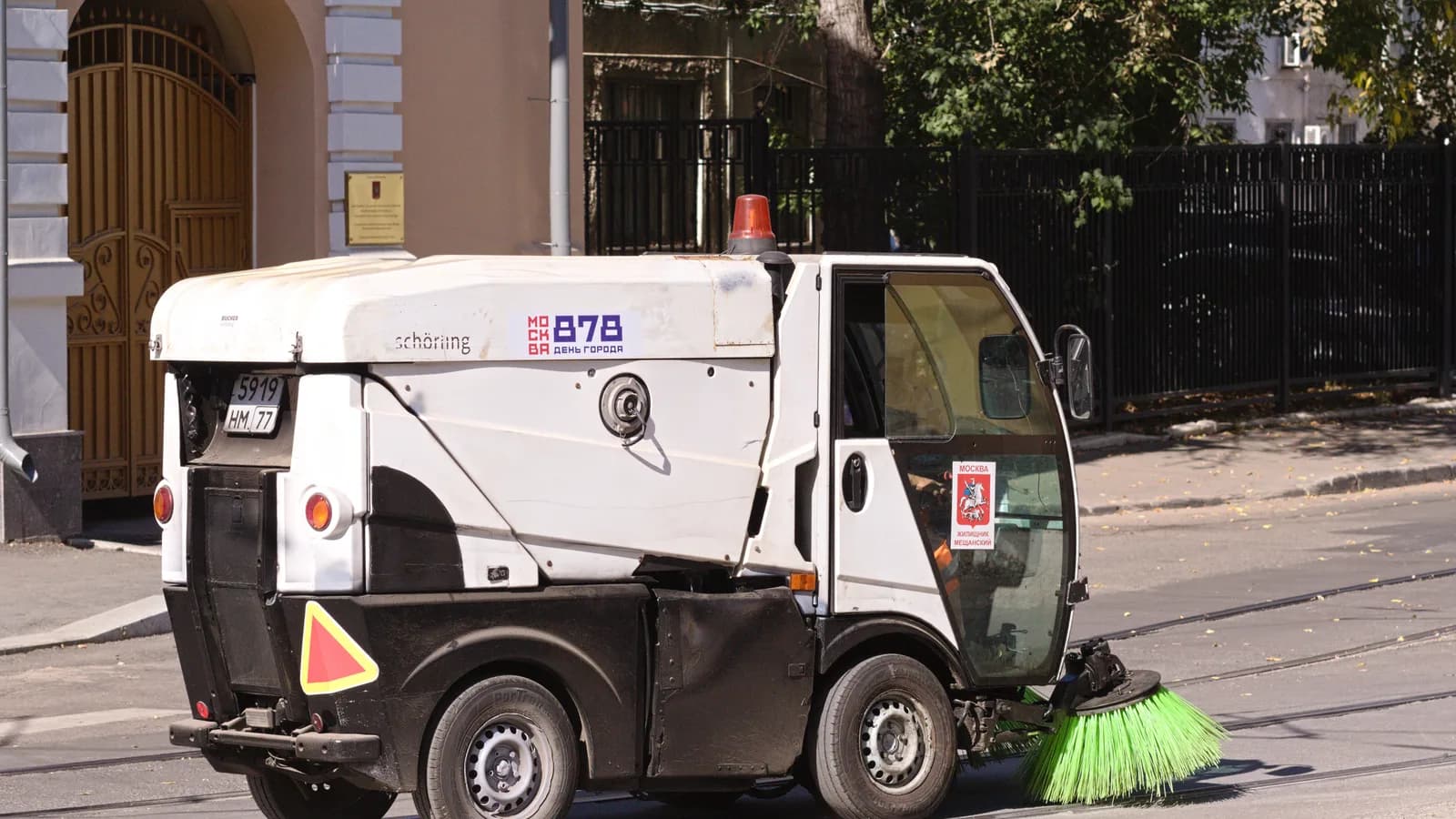 A compact street sweeper cleaning a curb lane