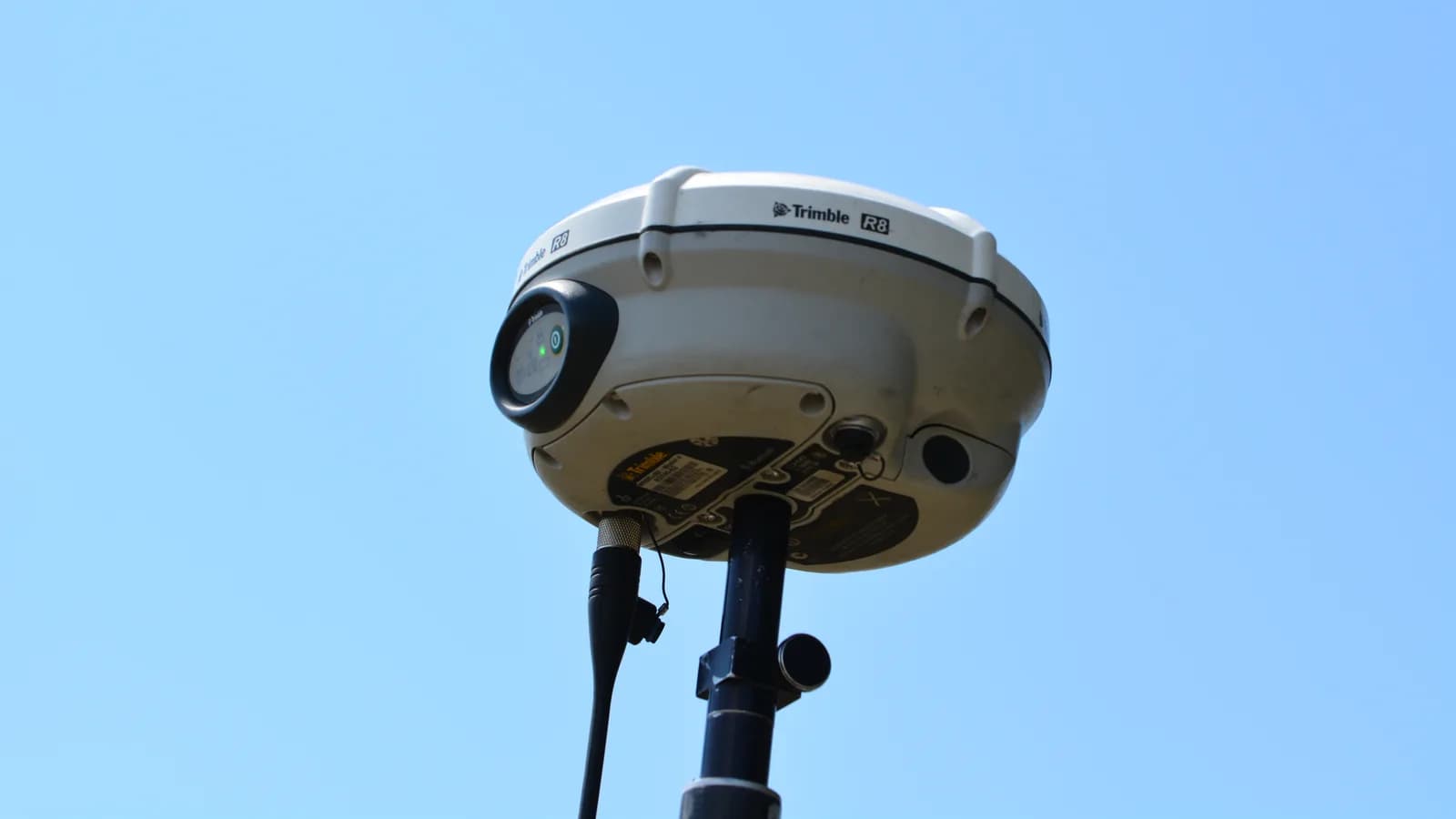 A GNSS survey receiver on a pole against a clear sky