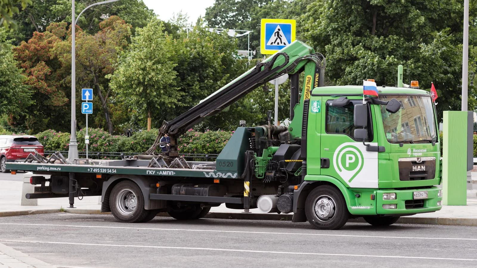 A green flatbed tow truck with its bed tilted, parked on a city street