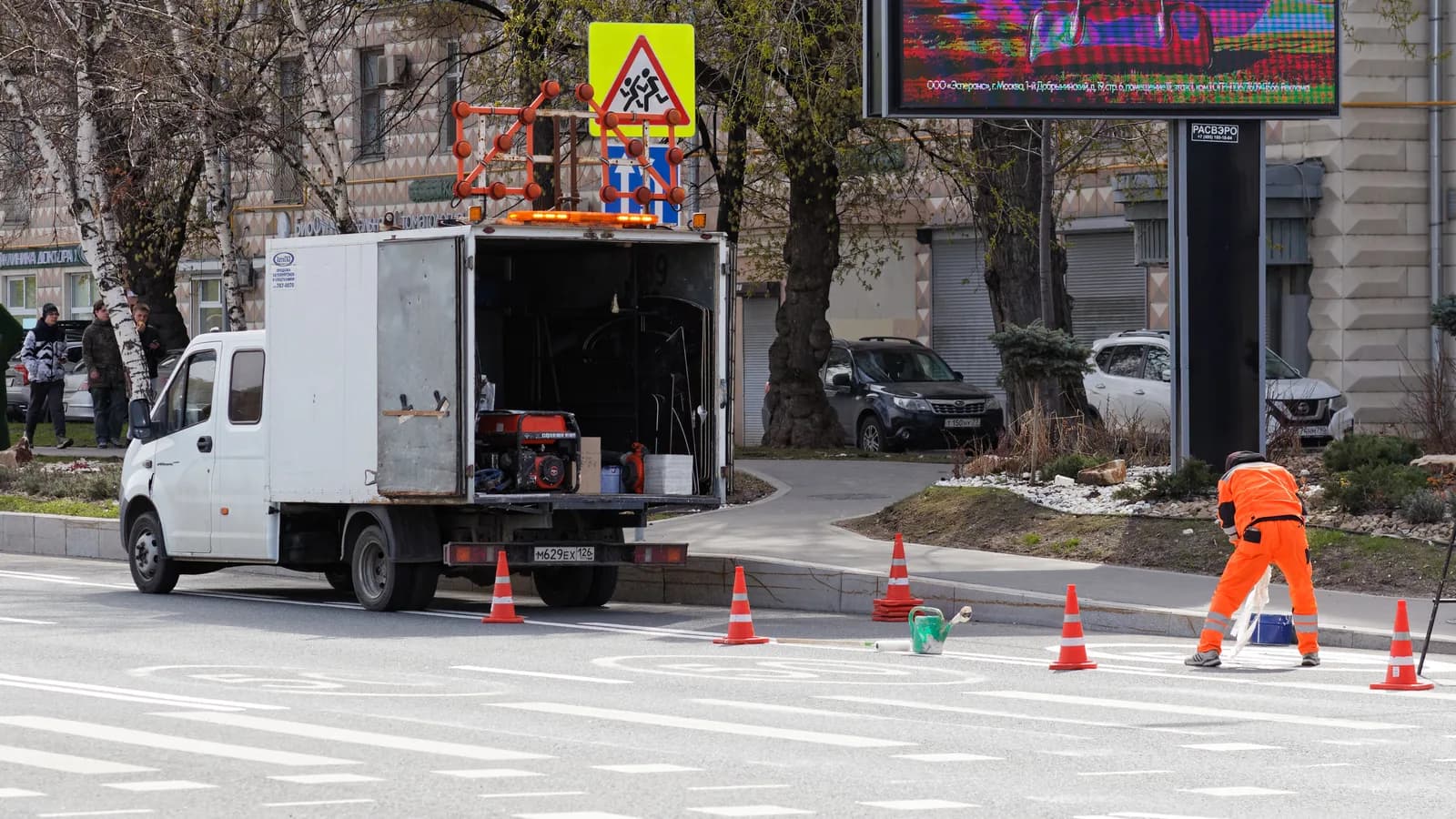 A road-marking crew truck with cones set out while a worker in orange paints lane lines
