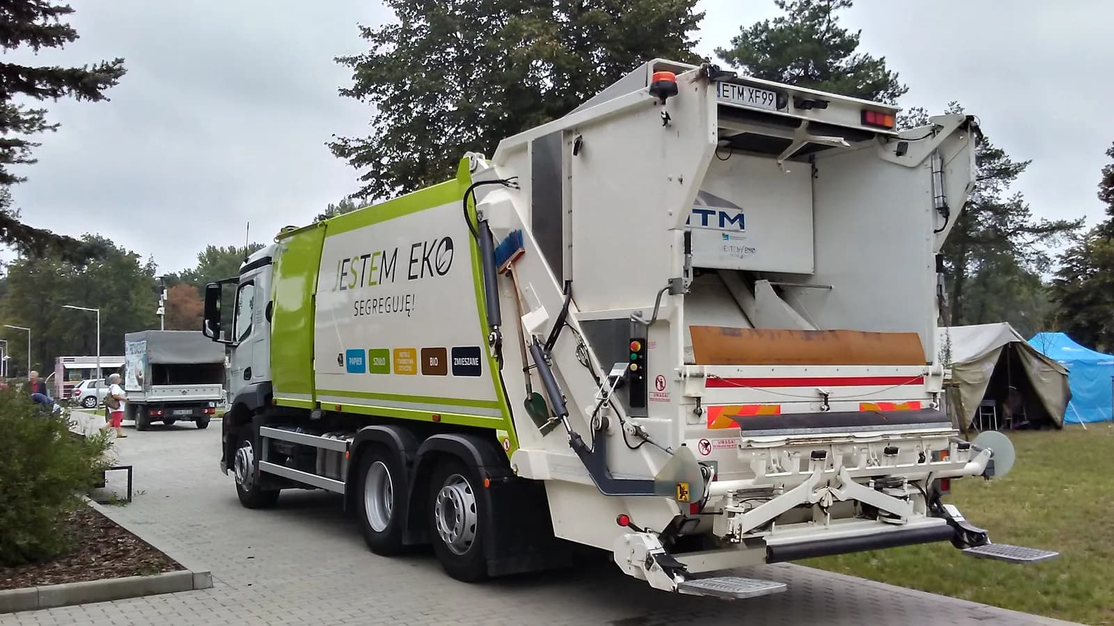 A white rear-loader garbage truck collecting bins on a residential street