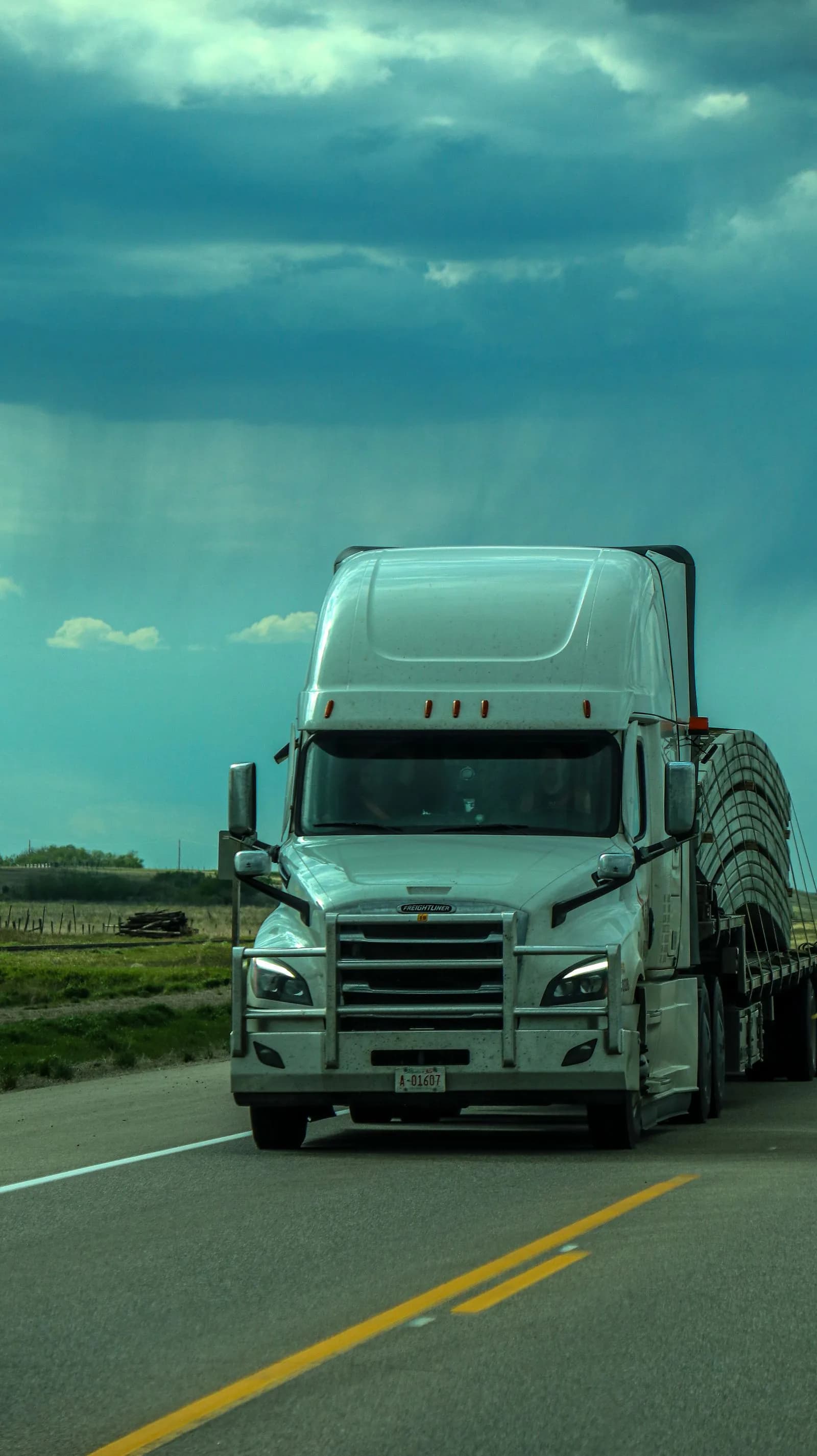 A white semi-truck traveling on a highway under a dramatic cloudy sky
