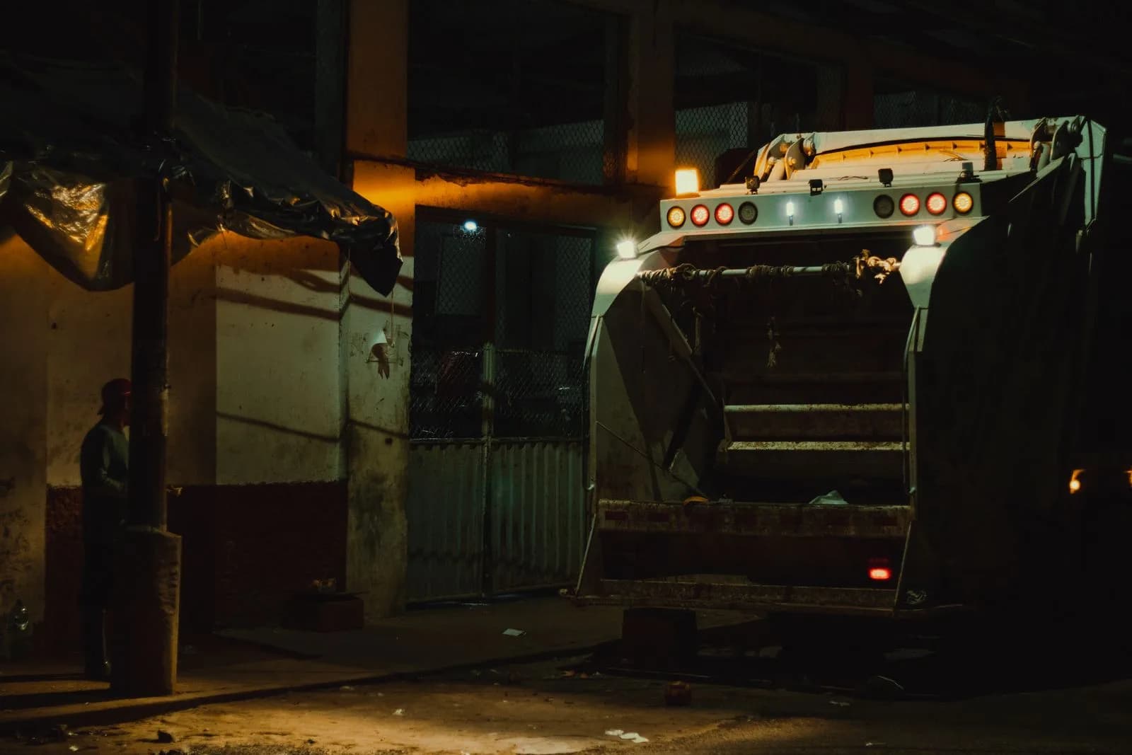 A heavy front-loader garbage truck servicing a commercial dumpster on a residential street