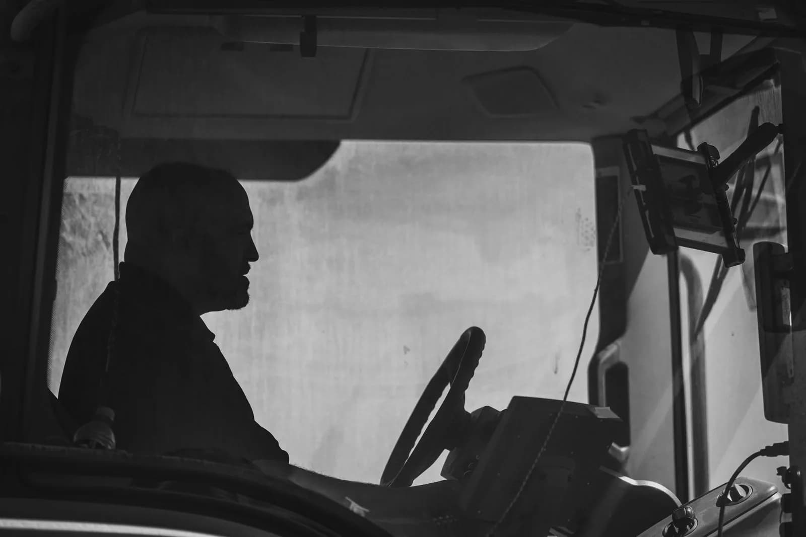 A commercial truck driver at the wheel with a road-facing telematics camera mounted on the windshield
