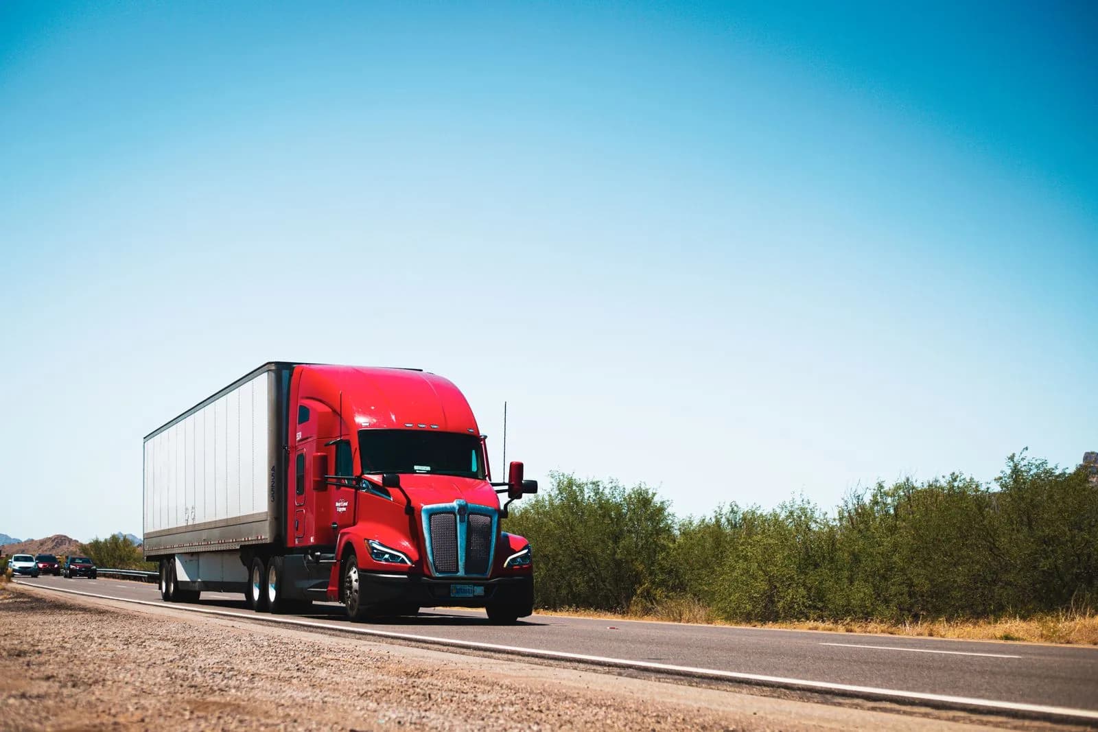 Red semi-truck traveling on an open highway under a clear blue sky