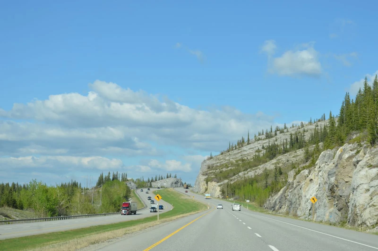 A highway cutting through rocky cliffs and forest near Drumheller, Alberta, with a semi truck on the road