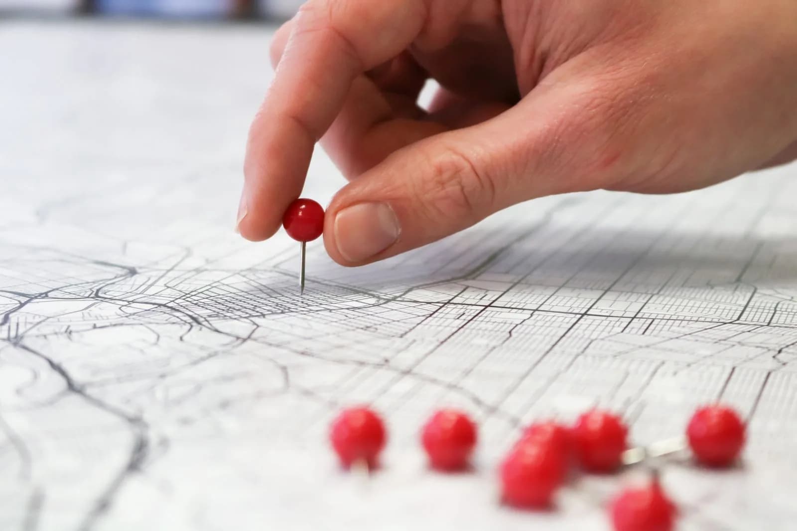 A hand placing a red pin marker on a printed street map