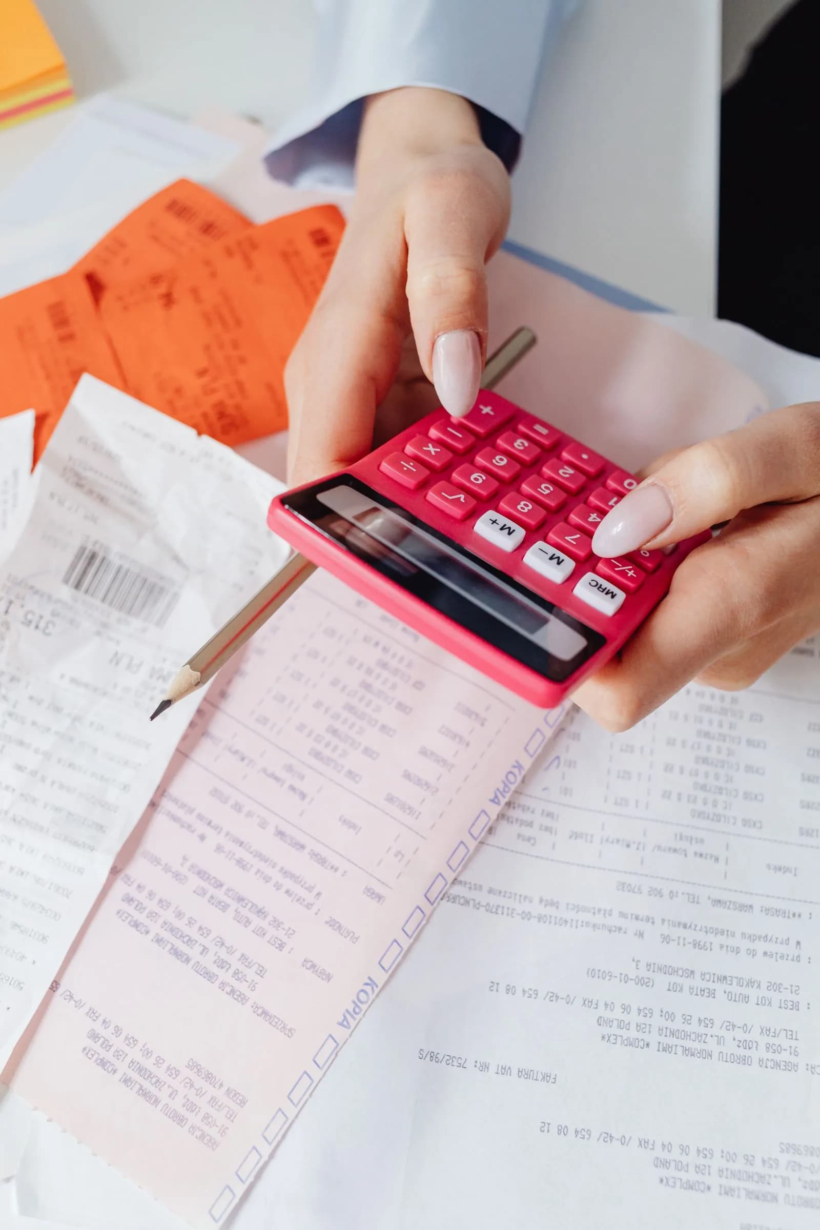 Hands using a calculator surrounded by financial receipts and paperwork