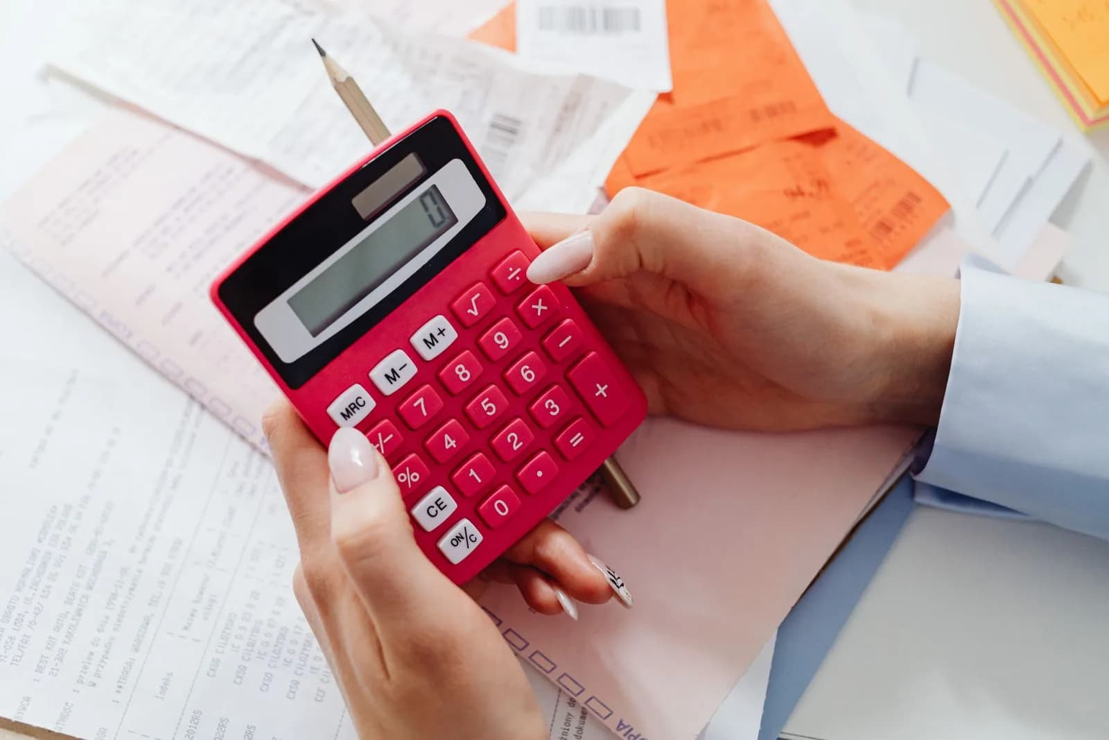 Hands holding a red calculator surrounded by receipts and financial documents