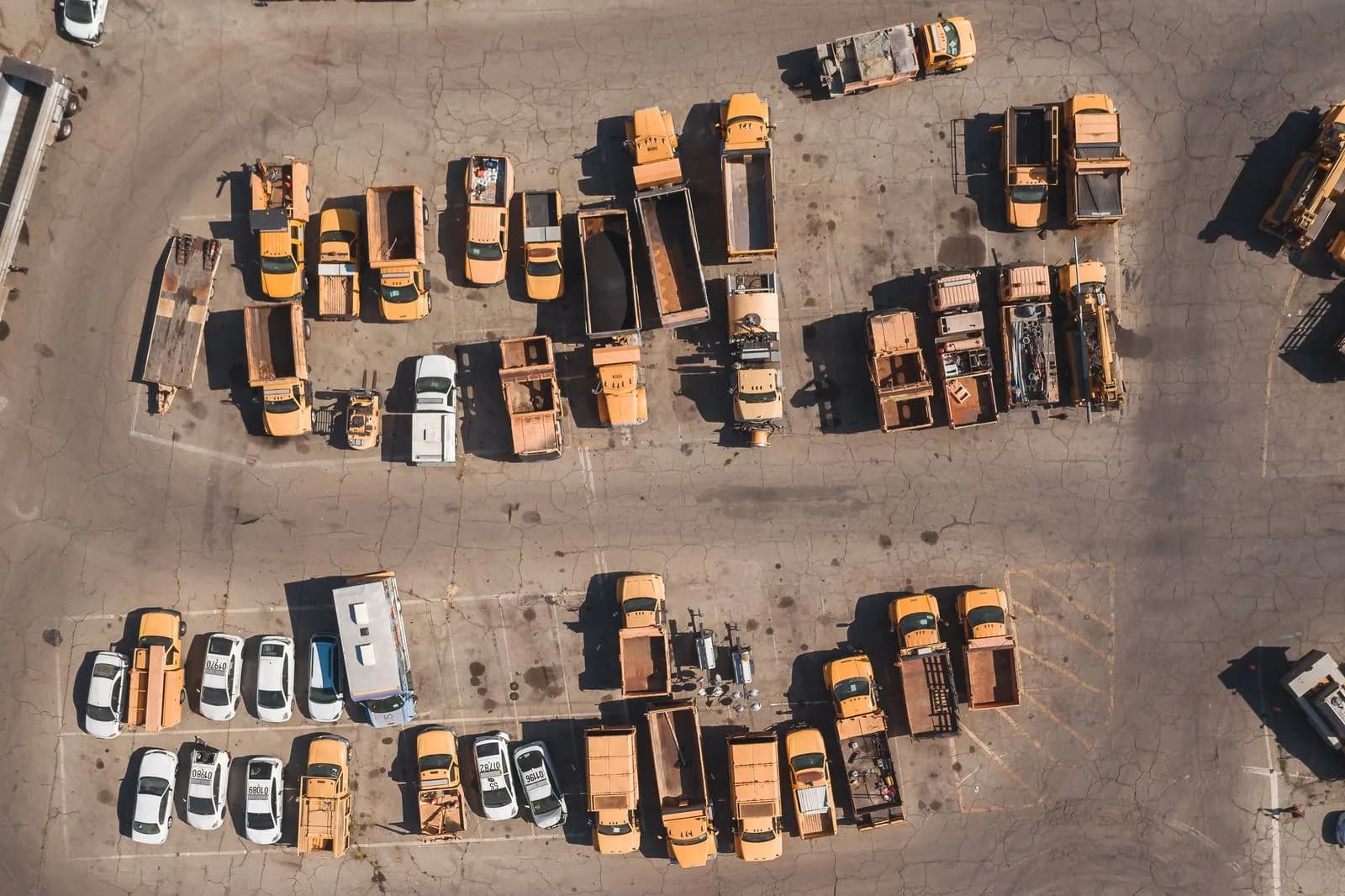 Aerial view of a municipal vehicle yard with a mix of service trucks and cars