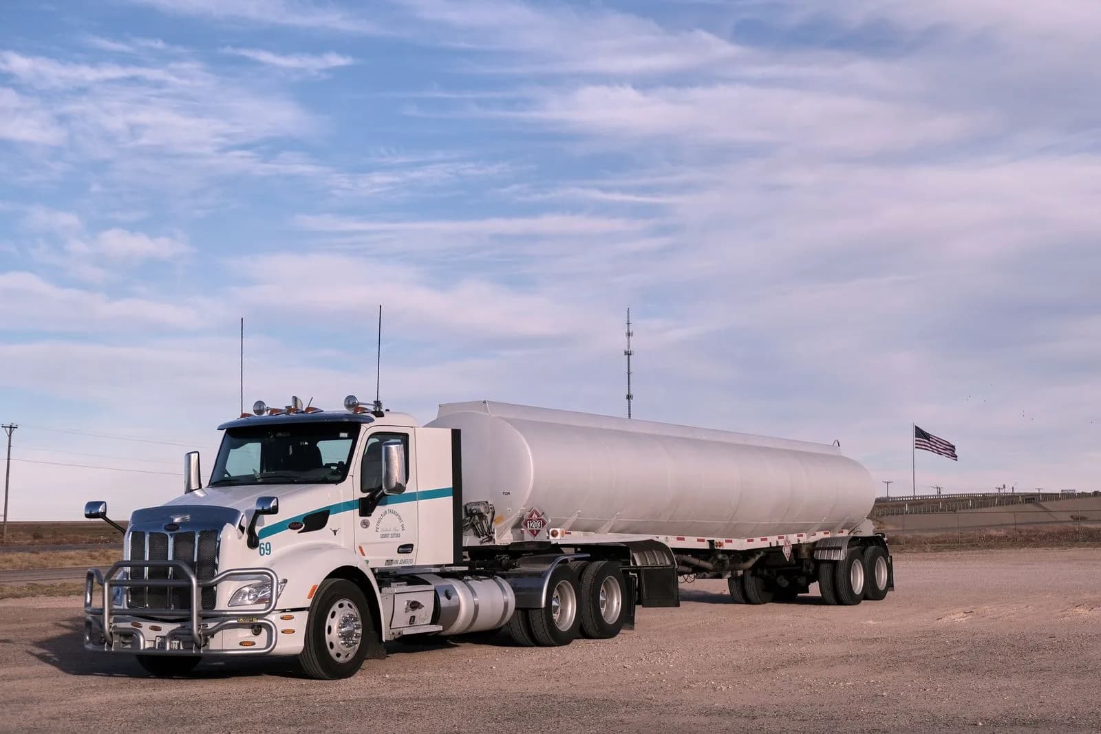 A white tank truck parked on a gravel lot under a wide open sky